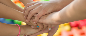 Eine Gruppe von Kindern, die sich an den Händen halten, wahrscheinlich in einem Spielbereich, mit bunten Spielzeugen im Hintergrund.