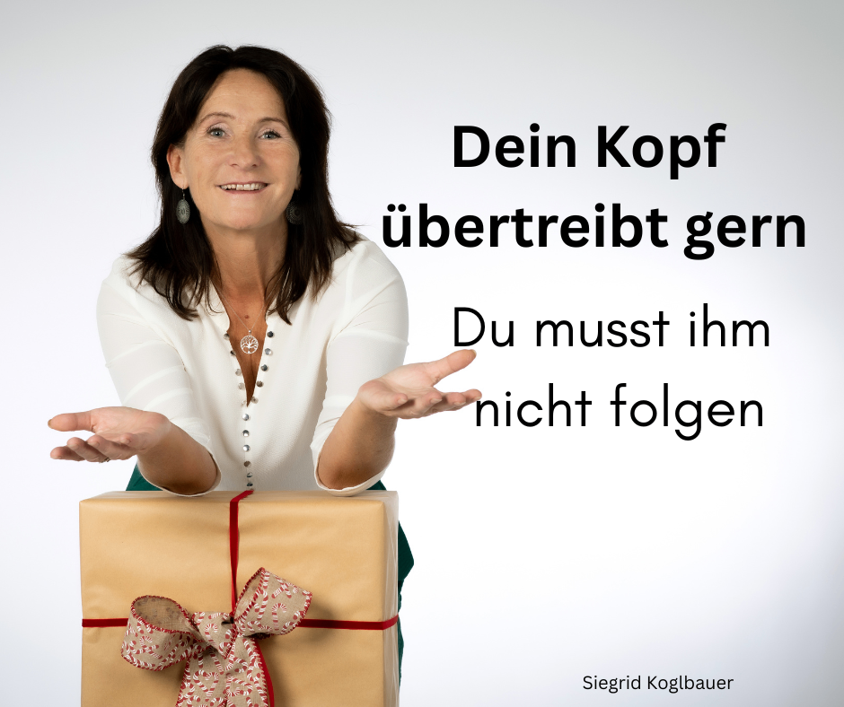 Eine lächelnde Frau hält eine Geschenkbox mit einer roten Schleife. Der Text auf dem Bild lautet 'Dein Kopf uebertreibt ger Du musst ihm nicht folgen'. Die Frau trägt eine weiße Bluse und grüne Hose. Das Bild hat einen Wasserzeichen, der 'Siegrid Koglbauer' lautet.