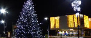 Ein Weihnachtsbaum ist nachts vor einem Gebäude mit blauen Lichtern beleuchtet. Das Gebäude hat Lichter und Text an seiner Wand.