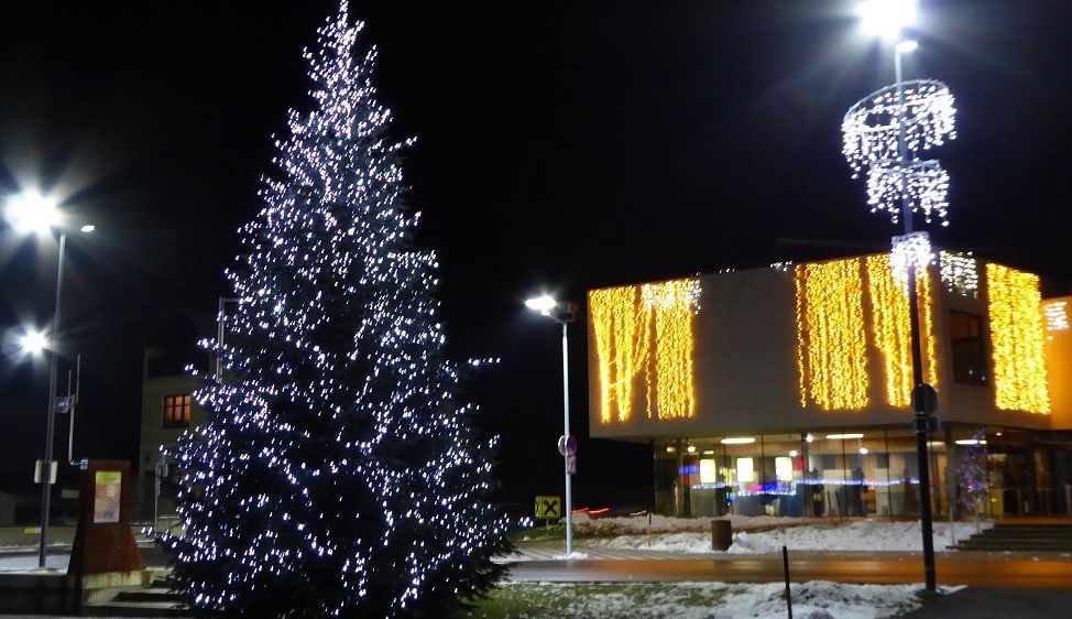 Ein Weihnachtsbaum ist nachts vor einem Gebäude mit blauen Lichtern beleuchtet. Das Gebäude hat Lichter und Text an seiner Wand.