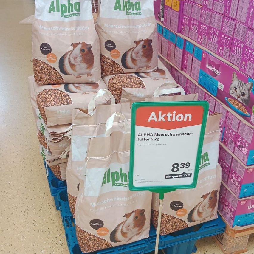 Ein Stapel von Alpha Meerschweinchenfutterbeuteln ist ausgestellt, mit einem Schild, das einen Rabatt von 8,39 anzeigt. Andere Haustierfutterprodukte sind im Hintergrund.