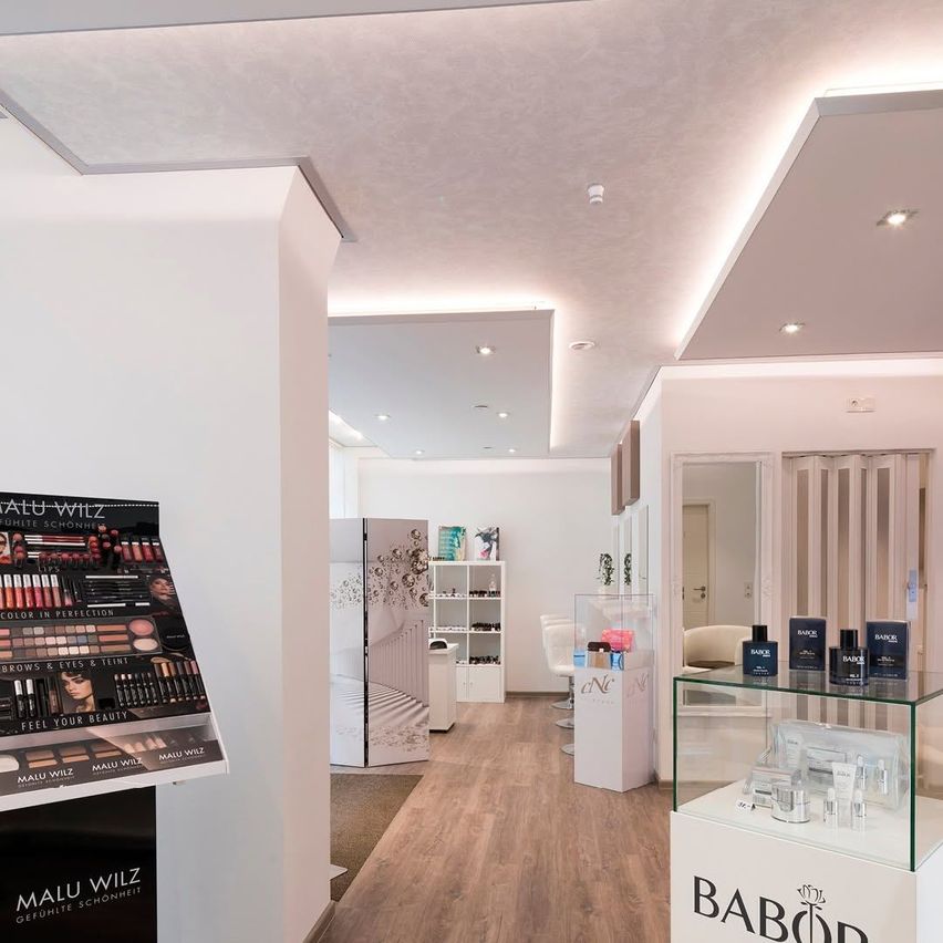 Interior of a beauty salon with wooden floors and white walls. A display for makeup products is on the left, and a glass case with Babor products is on the right.