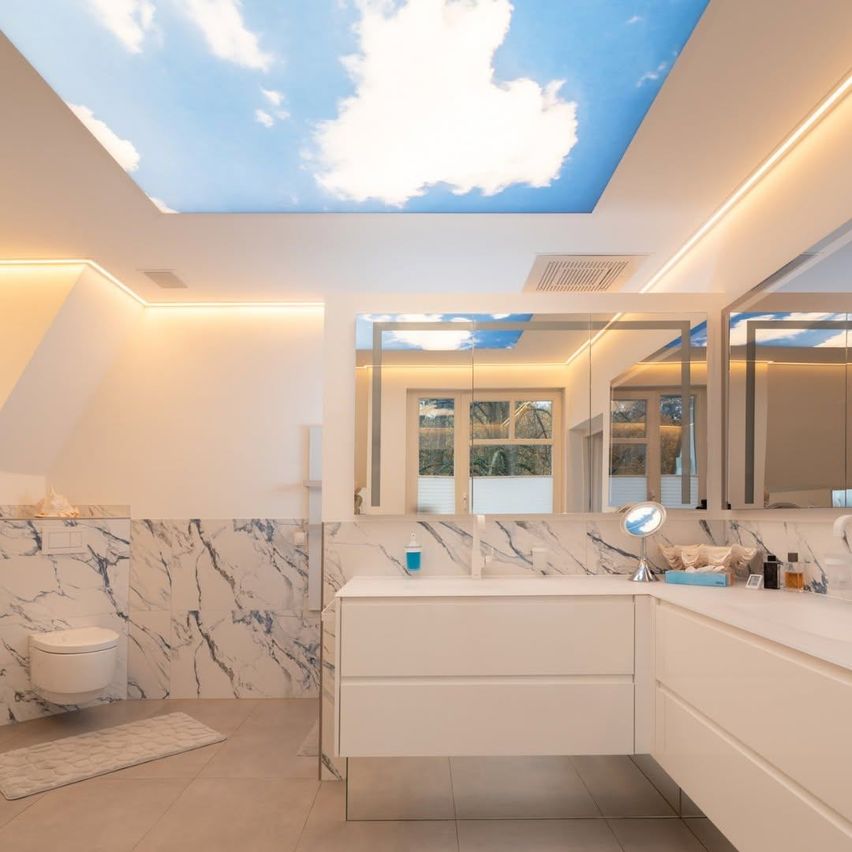 Ein modernes Badezimmer mit einer wolkenförmigen Decke, weißen Marmorwänden und einem weißen Waschbecken mit Spiegel. Der Boden hat einen Teppich und Fliesen, und auf der linken Seite befindet sich ein WC.