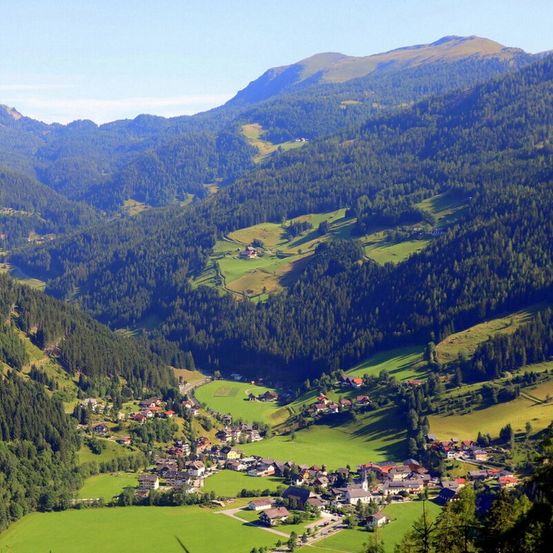 Ein Luftbild eines Tals mit grünen Feldern, Häusern und Bergen, die von Bäumen bedeckt sind.