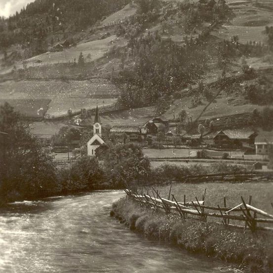 Ein Schwarz-Weiß-Foto zeigt ein ländliches Dorf mit einer kleinen Kirche und einem Fluss, der durch es fließt.