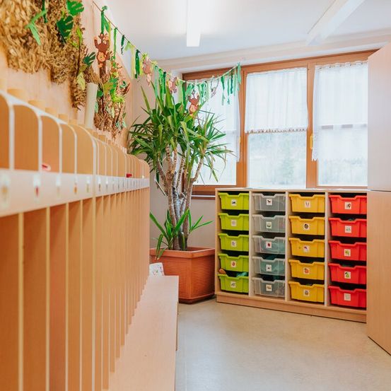 Ein Innenraum mit Holzregalen und Schubladen, die mit verschiedenen Gegenständen gefüllt sind. Ein großer Topf steht in der Ecke. Ein Fenster mit weißen Vorhängen befindet sich hinter dem Topf.