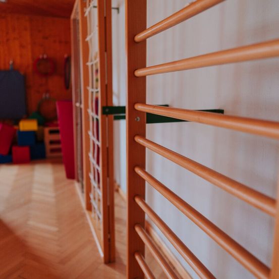 Nahaufnahme von Holzstangen an einer Wand in einem Spielzimmer mit Holzboden und Spielzeug im Hintergrund.