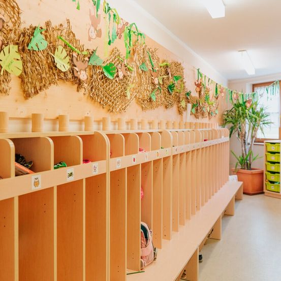 Eine Reihe von Holzschränken mit verschiedenen Gegenständen darin. Ein dekoratives Affen-Thema schmückt die Wand darüber. Ein Topf mit Pflanze steht rechts neben einem Fenster.