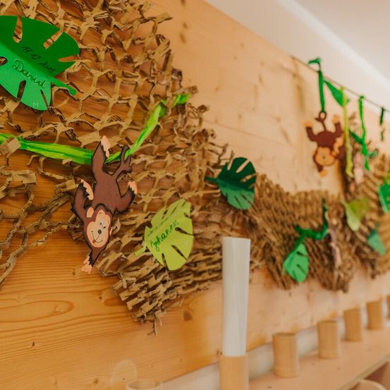 Eine Dschungel-Wanddekoration mit braunen und grünen Papierausschnitten, einschließlich Blätter, Affen und einem Banner mit dem Namen David. Eine weiße Kerze steht in der Mitte, umgeben von kleinen Bambusbechern.