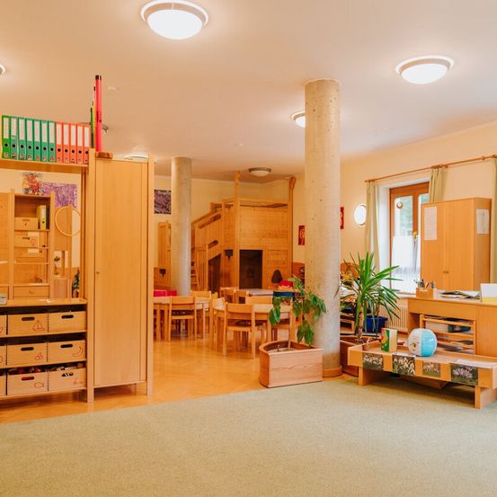 Ein Blick in das Innere eines Kinderzimmers mit Teppich, Holzmöbeln und Regalen. Ein Topf und ein Ball stehen auf dem Tisch.