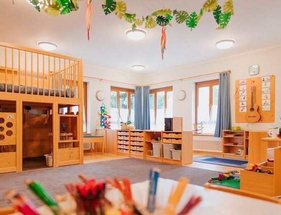 Ein gemütliches Kinderzimmer mit Holzbetten, Regalen, einem Tisch mit Spielzeug und farbenfrohen Dekorationen an der Decke.