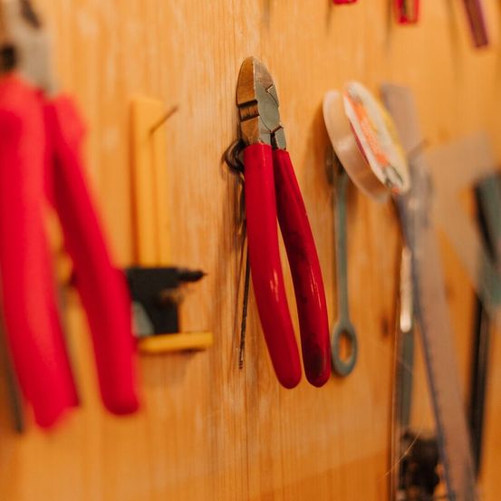 Eine Holzwand mit verschiedenen Werkzeugen, darunter rote Zangen, ein schwarzes Werkzeug, ein gelbes Werkzeug und eine Rolle Klebeband.