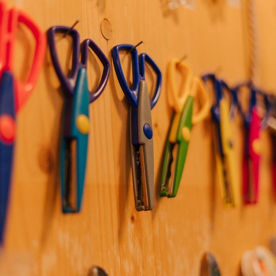 Eine Reihe bunter Scheren ist an einer Holzwand befestigt, jede mit unterschiedlichen Griffdesigns und Farben.