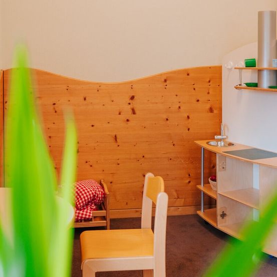 Ein kleiner, gemütlicher Raum mit Holzwand und -boden, einem kleinen Bett mit rot-weiß kariertem Bettzeug, einem Holzstuhl und einem kleinen Holzschreibtisch.