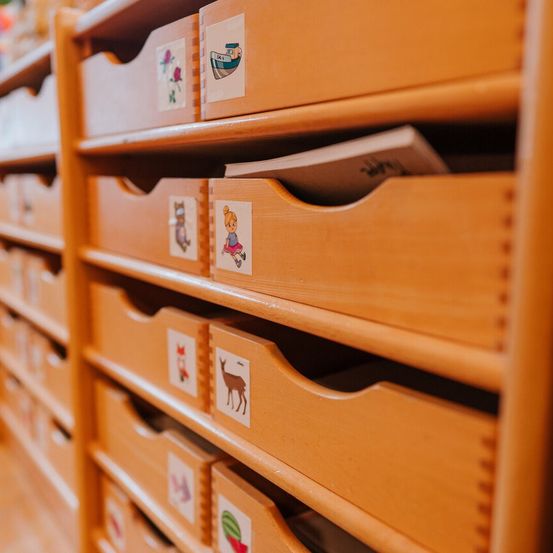 Nahaufnahme von Holzschubladen mit Etiketten, zeigt ein Buch in einer Schublade und verschiedene Illustrationen wie ein Boot, ein Mädchen, eine Katze, einen Hirsch und eine Wassermelone.