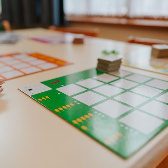 Ein Tisch hat ein grünes Gitter darauf, mit mehreren Karten, die gestapelt sind. Zwei andere Karten mit unterschiedlich gefärbten Gittern sind ebenfalls auf dem Tisch. Im Hintergrund befindet sich ein Fenster.