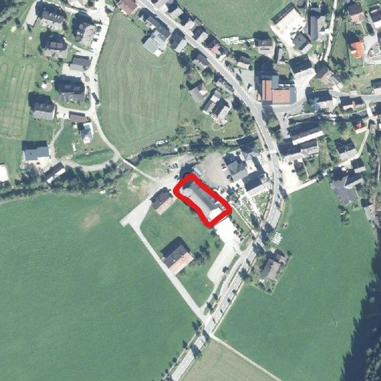 Luftaufnahme eines ländlichen Gebiets mit einer roten Linie, die ein Grundstück auf einem grünen Feld mit mehreren Gebäuden und Straßen hervorhebt.