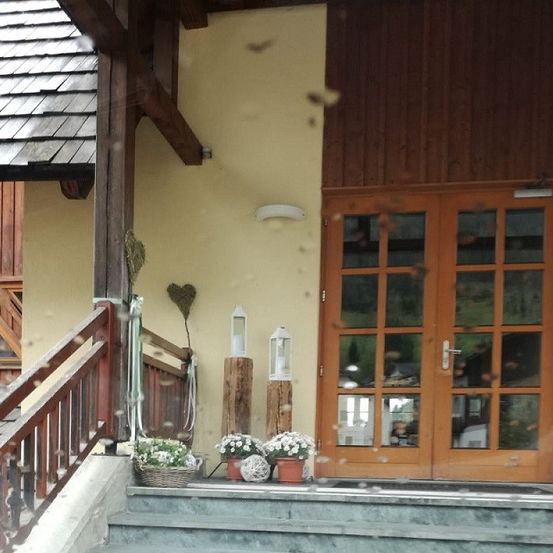 Ein Hauseingang mit einer Holztür, Stufen und dekorativen Gegenständen. Zwei weiße Laternen und ein Herz befinden sich an der Wand.