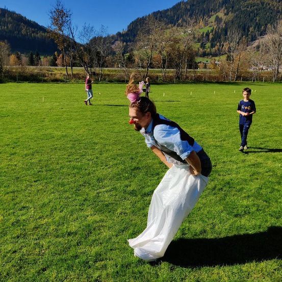 Ein Mann, der einen weißen Sack auf dem Rücken trägt, spielt in einem Grasfeld mit Bergen im Hintergrund ein Spiel.