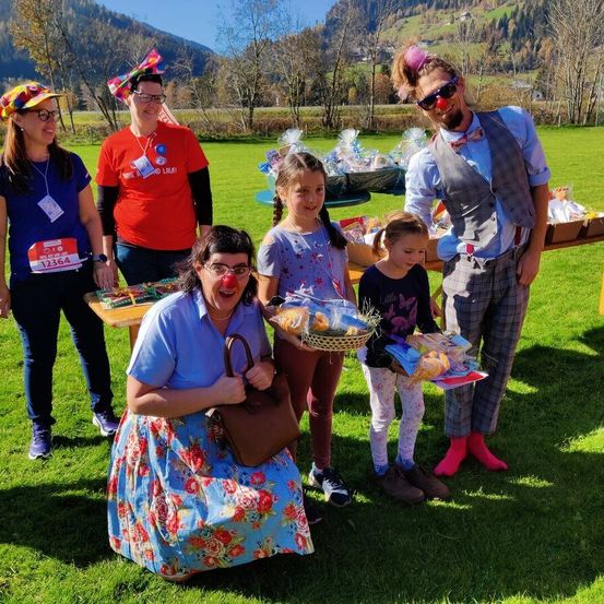 Eine Gruppe von Menschen in Kostümen posiert für ein Foto auf einer Wiese, wobei Kinder Körbe mit Essen halten und ein Mann mit Clownsnase.
