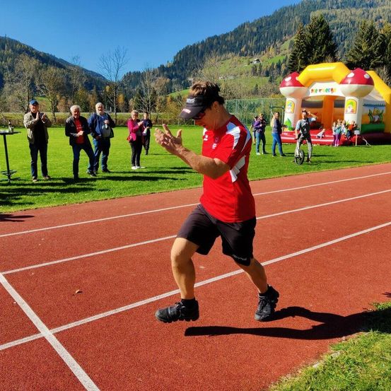 Ein Mann in einem roten Shirt und schwarzen Shorts führt eine Darbietung auf der Laufbahn vor, während Zuschauer zusehen.