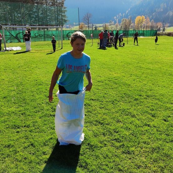 Ein Junge in einem blauen Shirt mit dem Aufdruck Los Angeles läuft mit einem Sack auf einem Sportplatz mit mehreren Leuten.