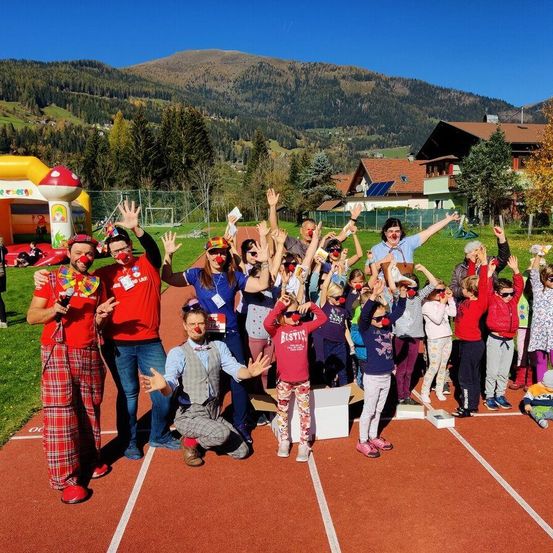 Eine Gruppe von Menschen in Clownkostümen posiert für ein Foto auf einer Laufbahn mit Bergen im Hintergrund.