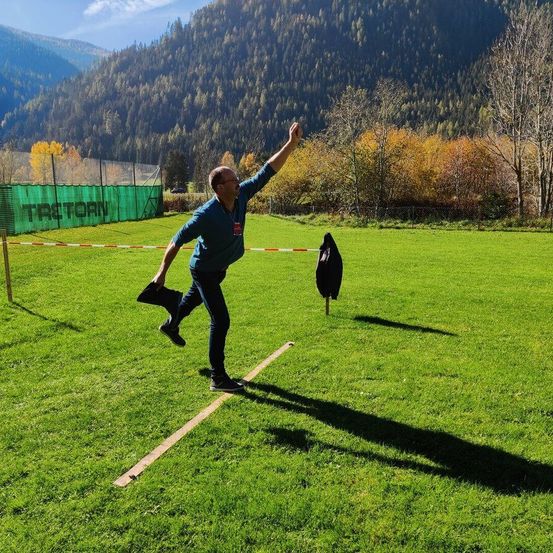 Ein Mann wirft einen Frisbee auf einem Rasenfeld mit Bergen im Hintergrund.