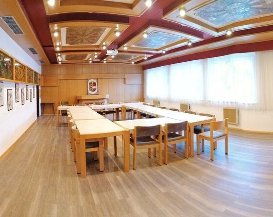 Ein leerer Konferenzraum mit Holzböden und -wänden. Lange Tische und Stühle sind in Reihen angeordnet. Kunstwerke und ein gerahmtes Bild sind an den Wänden montiert.