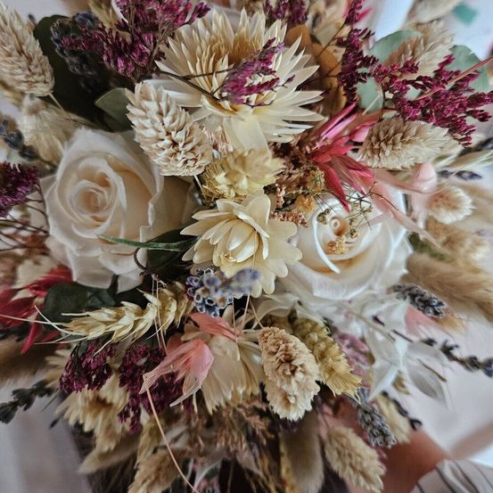 Ein Brautstrauß mit weißen Rosen, getrockneten Blumen und Grünzeug, nah aufgenommen.