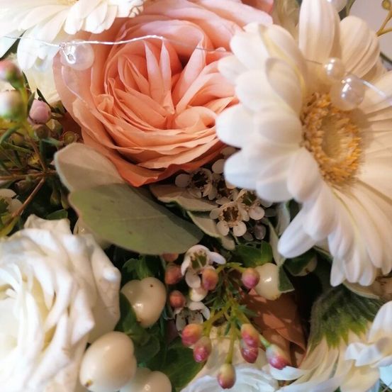 Eine Nahaufnahme einer Blumenarrangement mit Rosen, Gänseblümchen und anderen Blumen. Das Arrangement enthält eine zarte Perlenschnur.