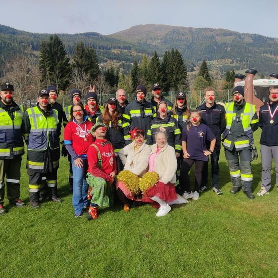 Eine Gruppe von Menschen in Clowns-Make-up posiert für ein Foto auf einem Rasenfeld mit Bergen im Hintergrund.
