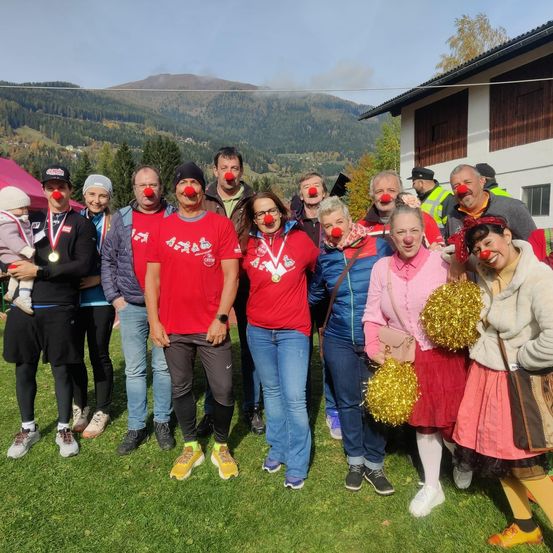 Eine Gruppe von Menschen mit roten Nasen posiert für ein Foto auf einer Rasenfläche mit Bergen im Hintergrund.