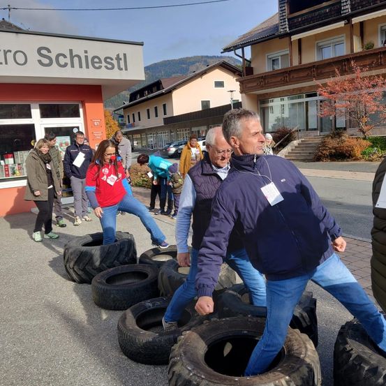 Eine Gruppe von Menschen geht auf Reifen in einer Freiluftumgebung, mit einem Gebäude namens 'Schie' im Hintergrund.