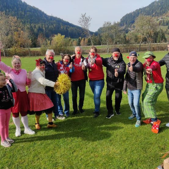 Eine Gruppe von Menschen, die Rot tragen und Clownsnasen tragen, posiert für ein Foto auf einem Grasfeld mit Bergen im Hintergrund.