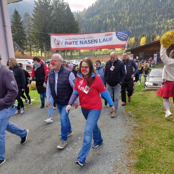 Eine Gruppe von Menschen mit roten Clownsnasen und roten T-Shirts läuft auf einem Pfad, wahrscheinlich an einer Wohltätigkeitsveranstaltung teilnehmend.