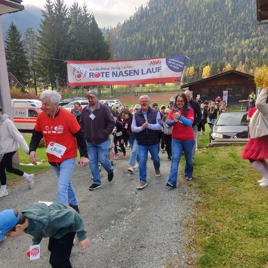Teilnehmer eines Wohltätigkeitslaufs, in roten Hemden und roten Luftballons, laufen einen Pfad hinunter, über dem ein Banner hängt.