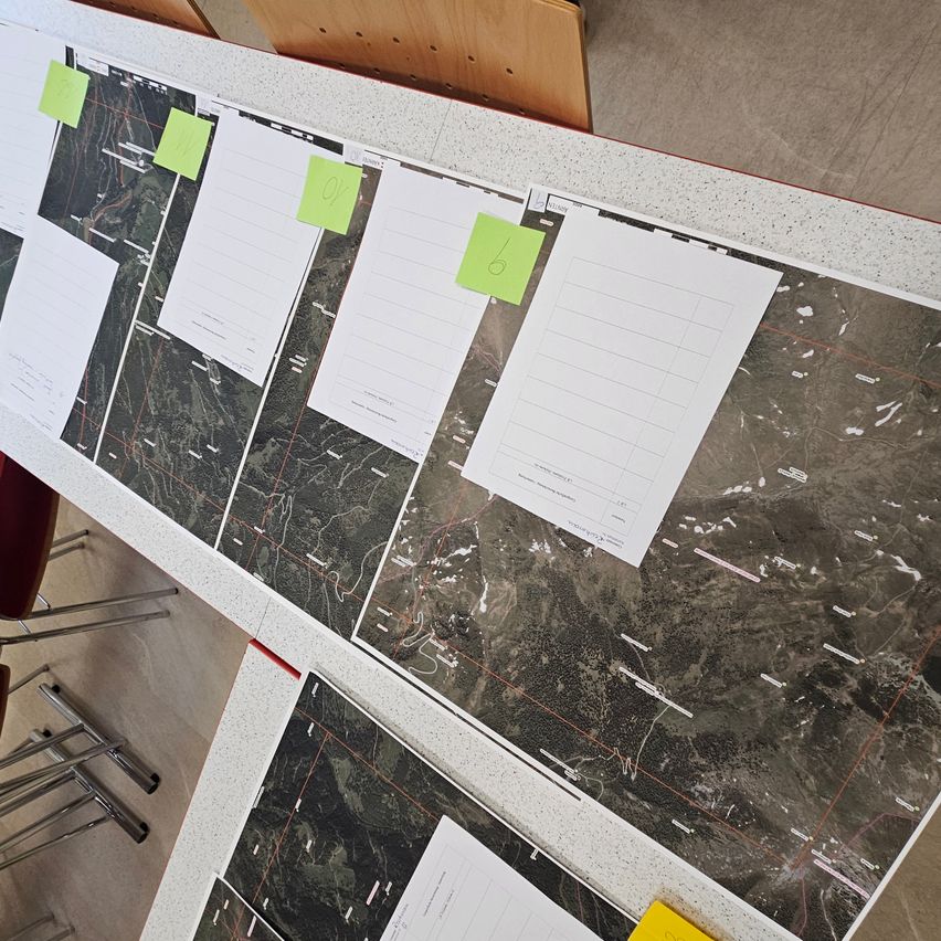 Eine Reihe von Karten liegt auf einem Tisch verteilt, mit Notizen und Markierungen. Mehrere Blätter Papier sind an den Karten befestigt.