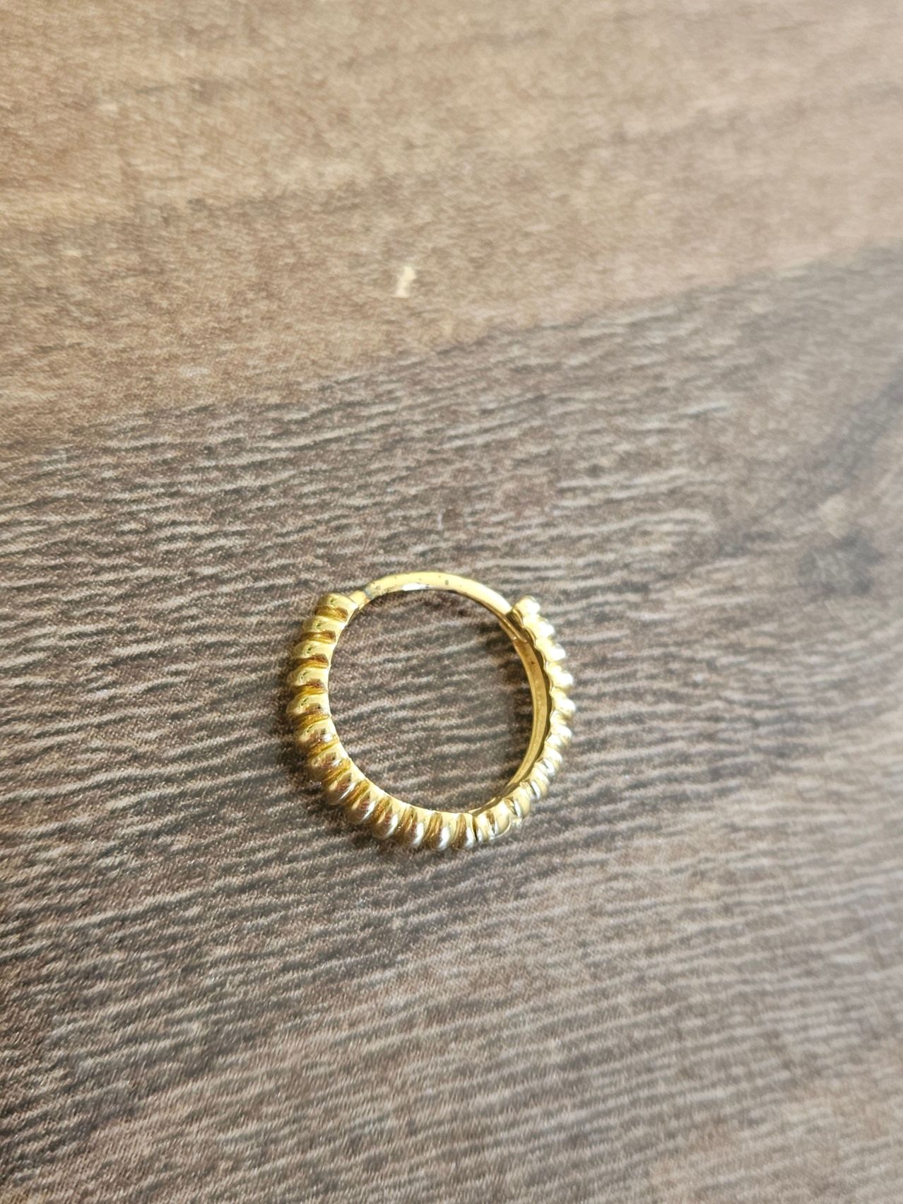 A small, gold-plated ring with a textured surface, resting on a wooden surface.