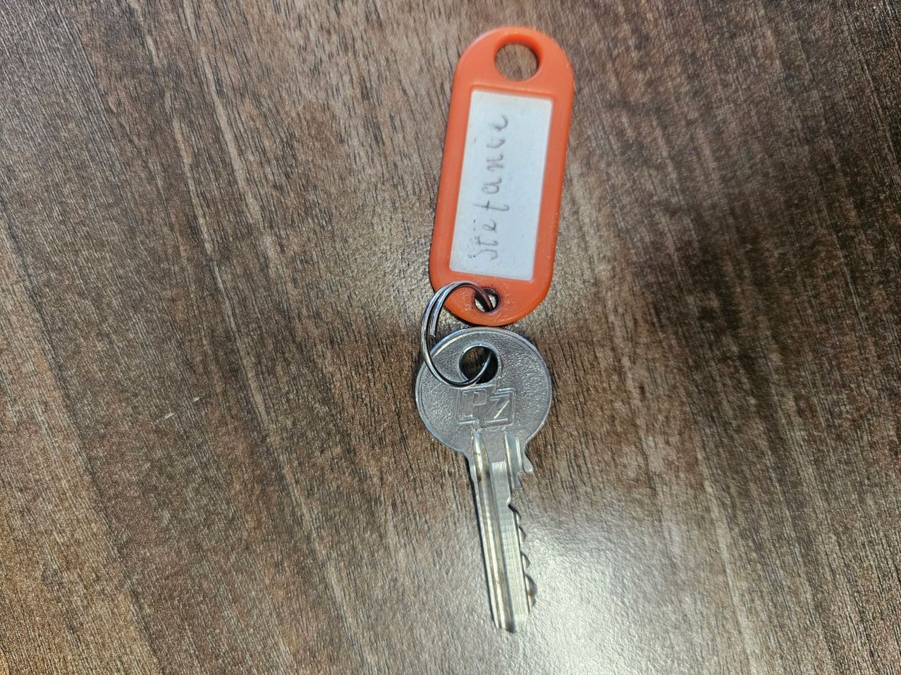 Ein Schlüssel mit einem orangefarbenen Etikett, beschriftet mit 'Residenz', liegt auf einer Holzoberfläche.
