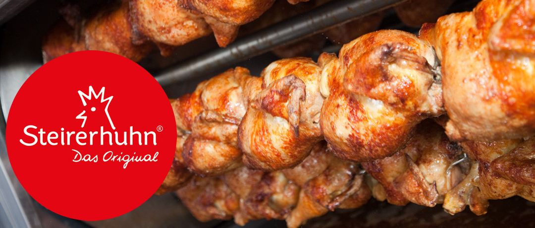 Nahaufnahme von Hähnchenstücken an Haken hängend, goldbraun und knusprig, mit einem roten Kreislogo unten links.