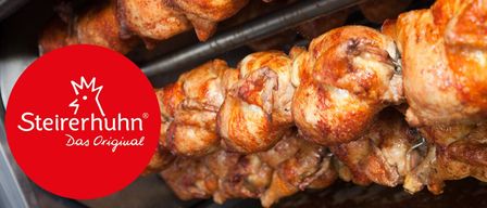 Ein Nahaufnahme von mehreren gebratenen Hühnern auf einem Grill. Die Hühner sind goldbraun mit knuspriger Haut, und einige haben ihre Köpfe noch dran. Das Bild zeigt ein Markenlogo in der unteren linken Ecke.