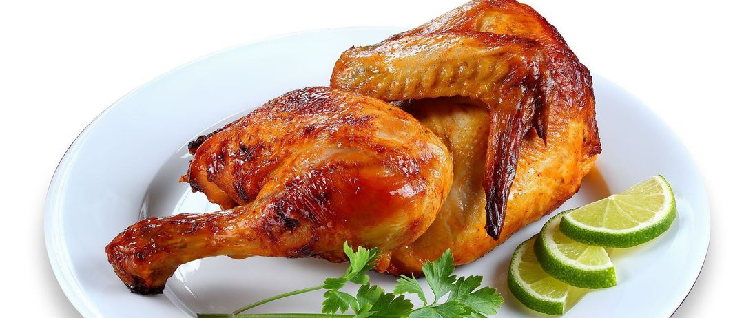Ein weißer Teller mit einem gebratenen Hähnchenschenkel und -flügel, garniert mit Petersilie und Limettenscheiben.