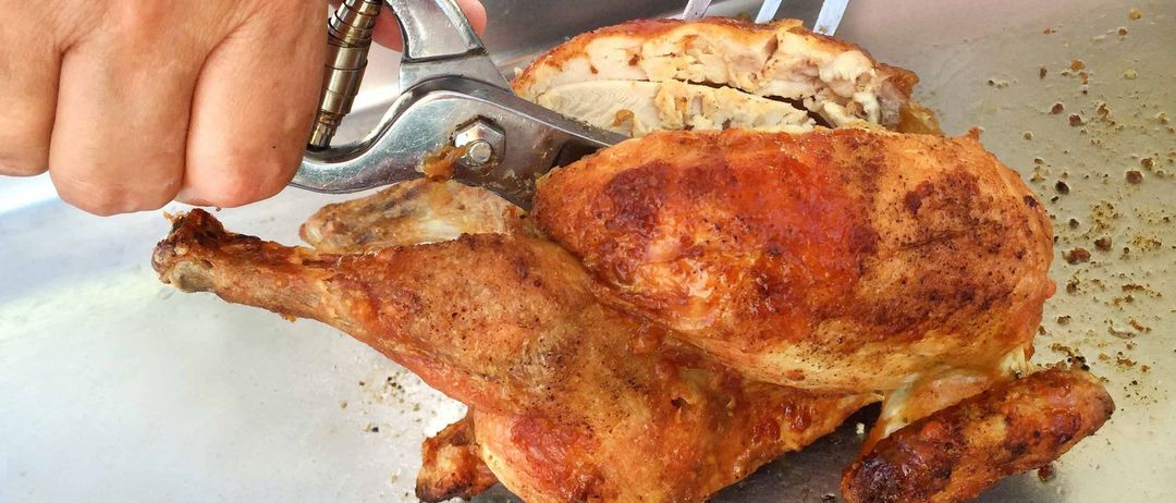 Eine Person schneidet ein gebratenes Huhn mit einer Metallzange, das Huhn hat eine knusprige Haut und der Hintergrund hat ein grünes und Herzdesign.