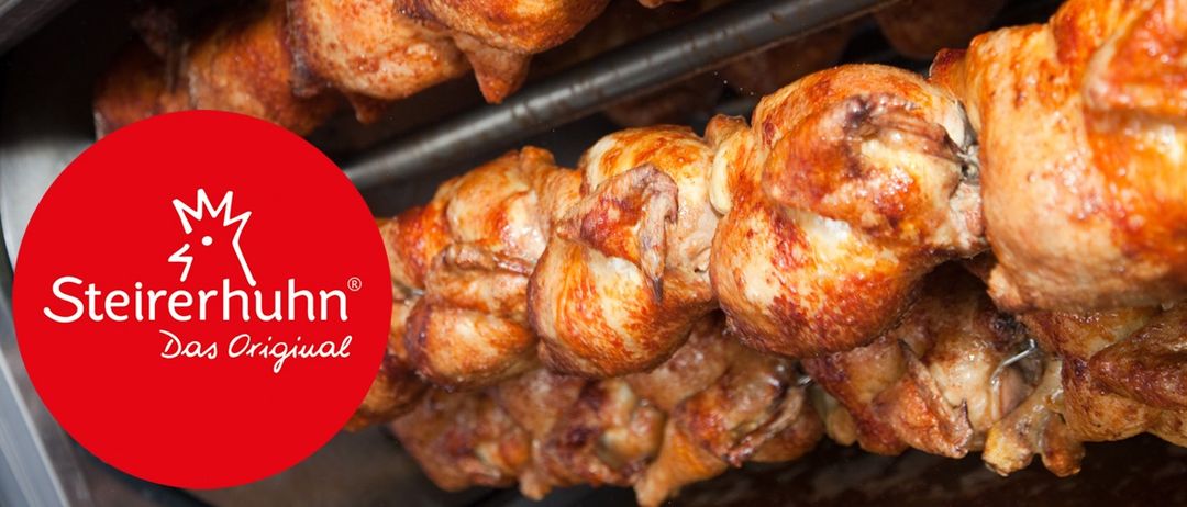 Nahaufnahme von ganzen, gebratenen Hähnchen auf einem Grill mit einem roten Kreislogo in der linken Ecke.