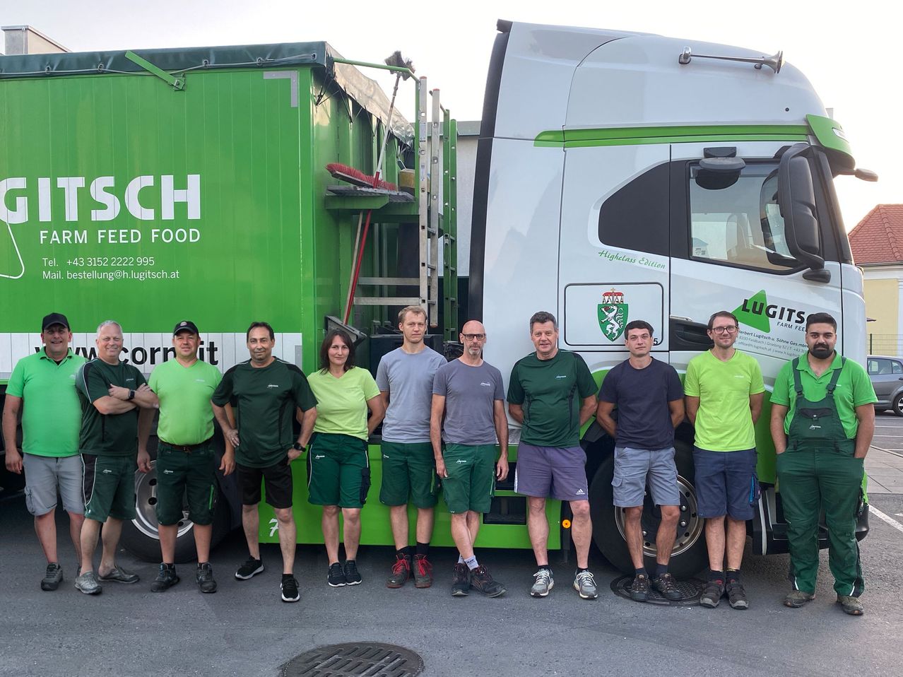 Eine Gruppe von Männern und Frauen in grünen und grauen Uniformen steht vor einem grünen Lastwagen mit dem Wort SCH darauf. Sie alle lächeln und scheinen für ein Foto zu posieren.