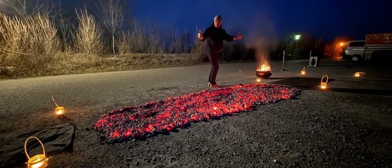 Eine Person steht bei Nacht auf einer Straße mit einem Feuer und mehreren brennenden Laternen auf dem Boden.