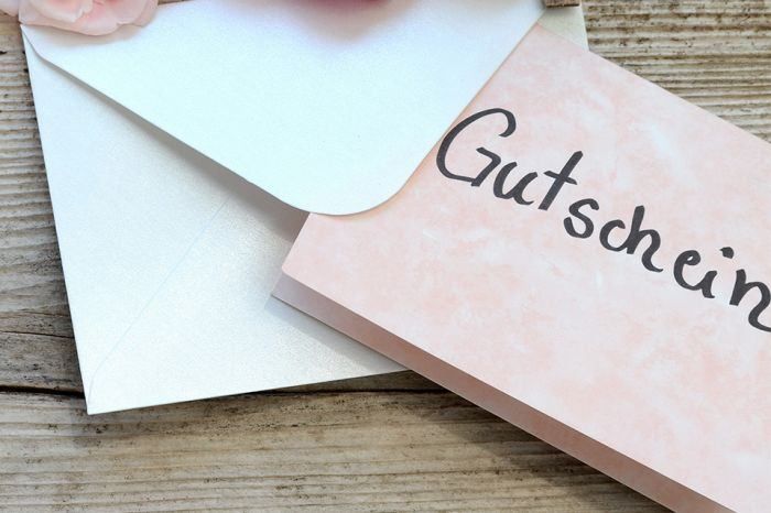 Eine rosa Karte mit dem Wort Gutschein darauf ist in einem Umschlag auf einer Holzoberfläche.