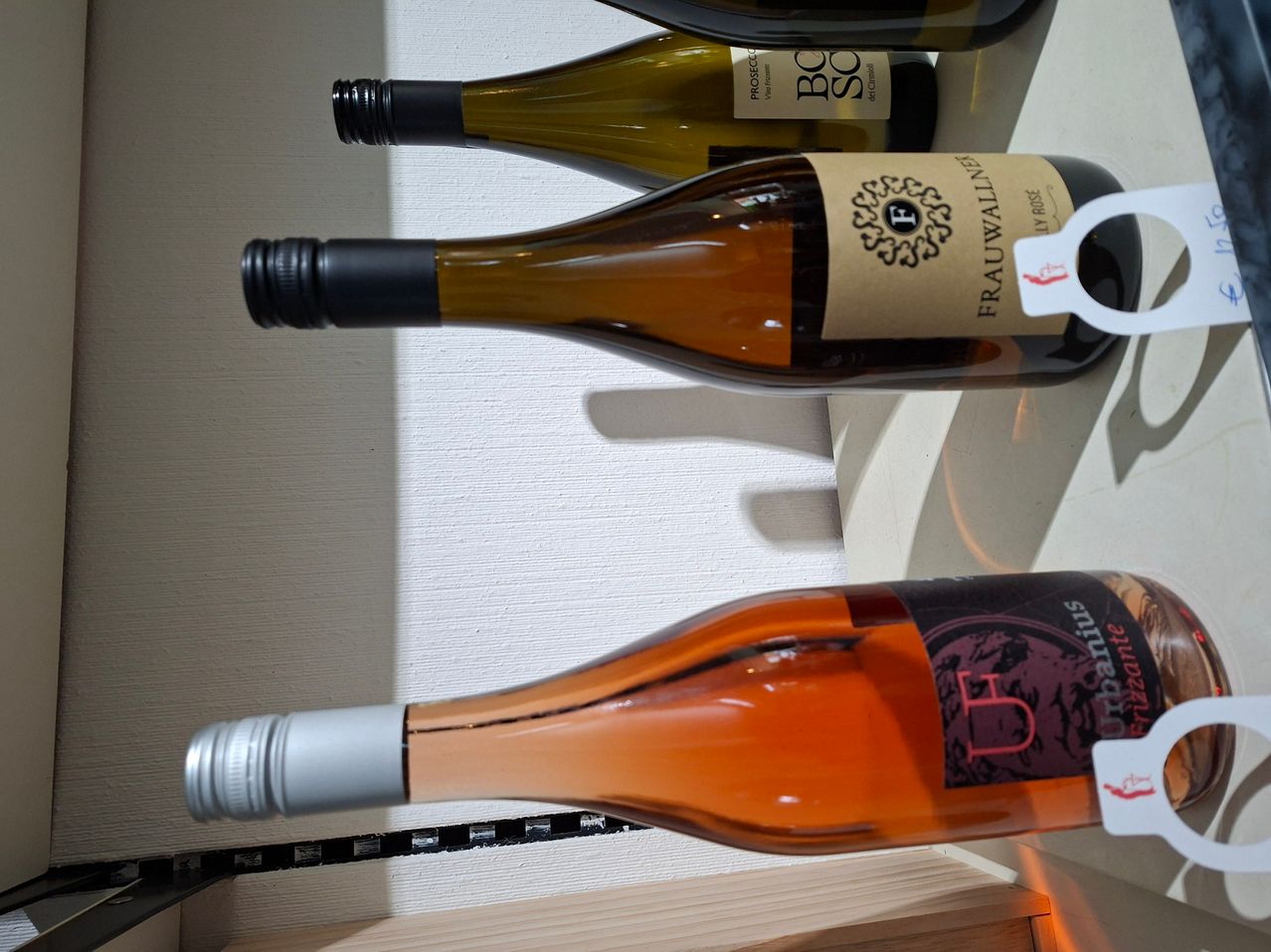 Drei Weinflaschen, die auf einer weißen Oberfläche gestapelt sind, eine mit einem Etikett, das Frauwallner liest, und eine andere mit einem Schild, das Bacchus liest.
