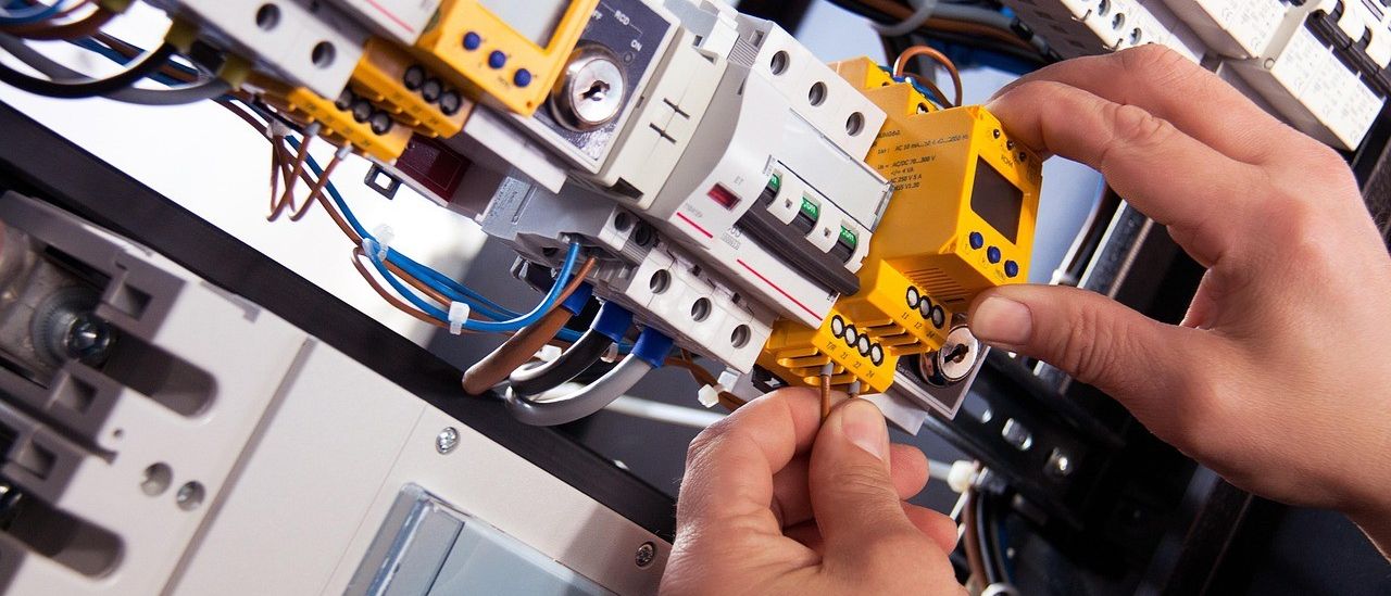 Eine Person justiert einen gelben Leistungsschalter in einem elektrischen Schaltschrank, umgeben von Kabeln und anderen Komponenten.